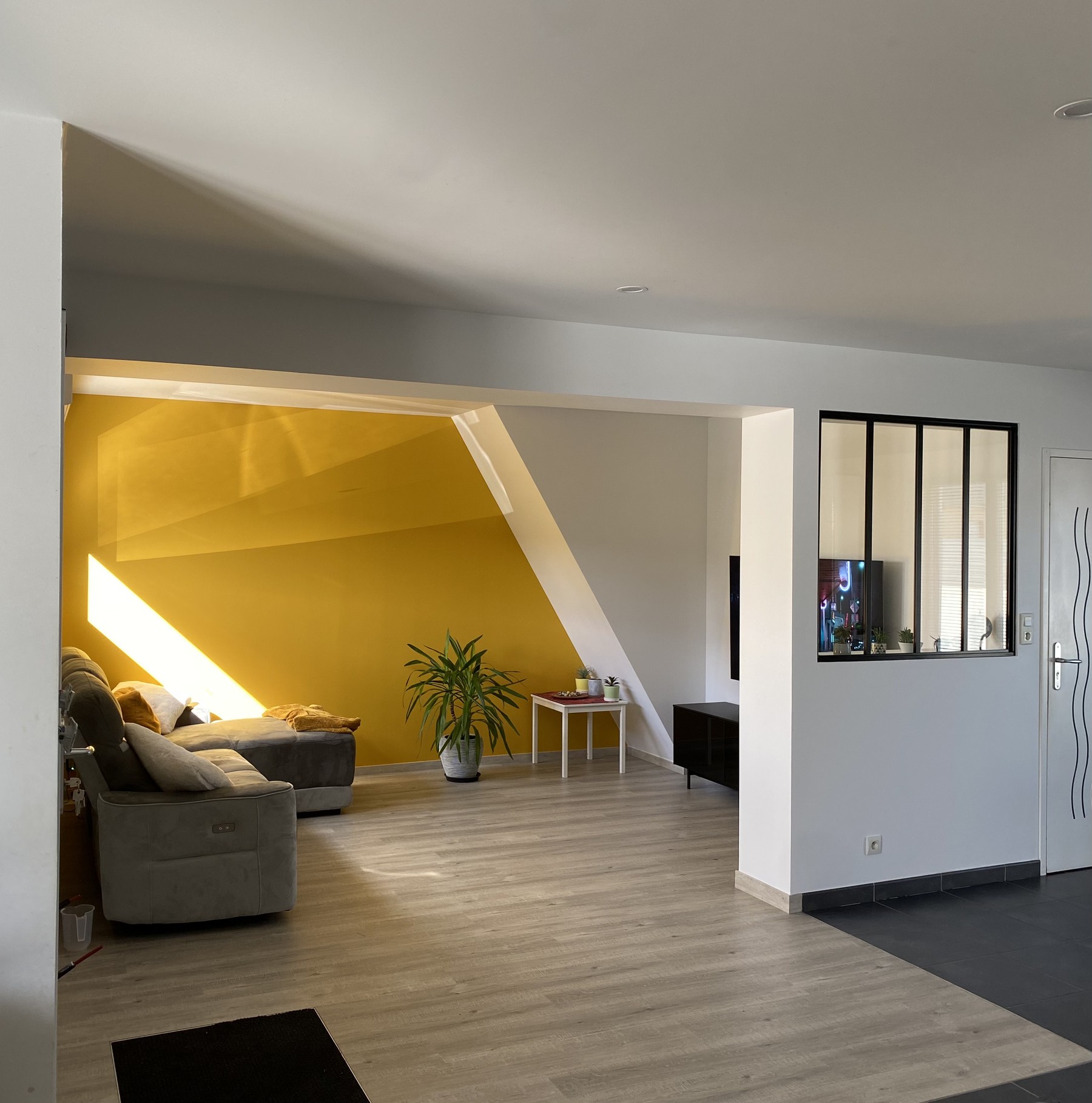 Salon contemporain peint dans une teinte jaune ocre par Artipeintre, parquet bois et verrière noire